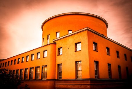 Rund, orange byggnad med fönster och en mörk himmel i bakgrunden.